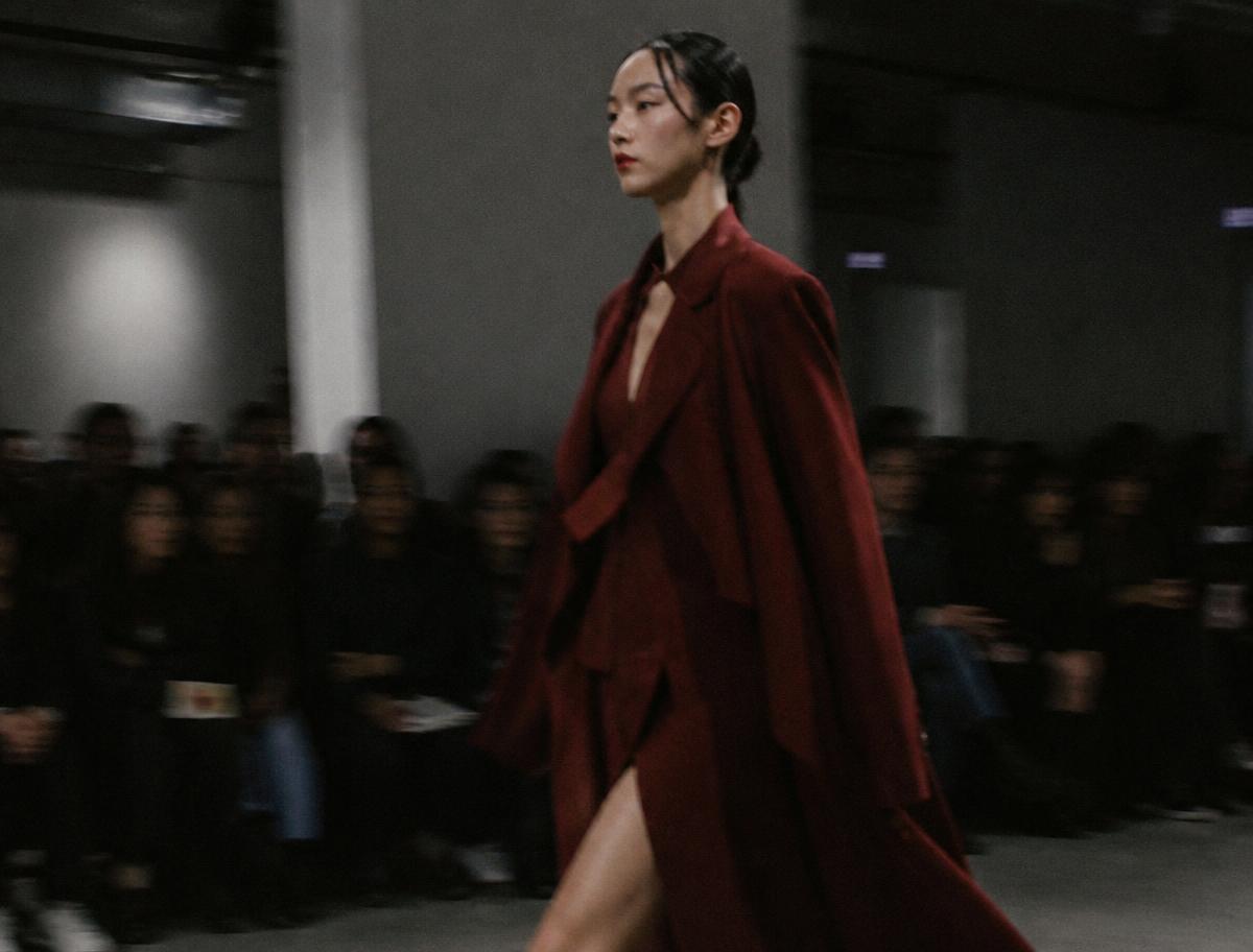 Model walking a runway in a deep red coat